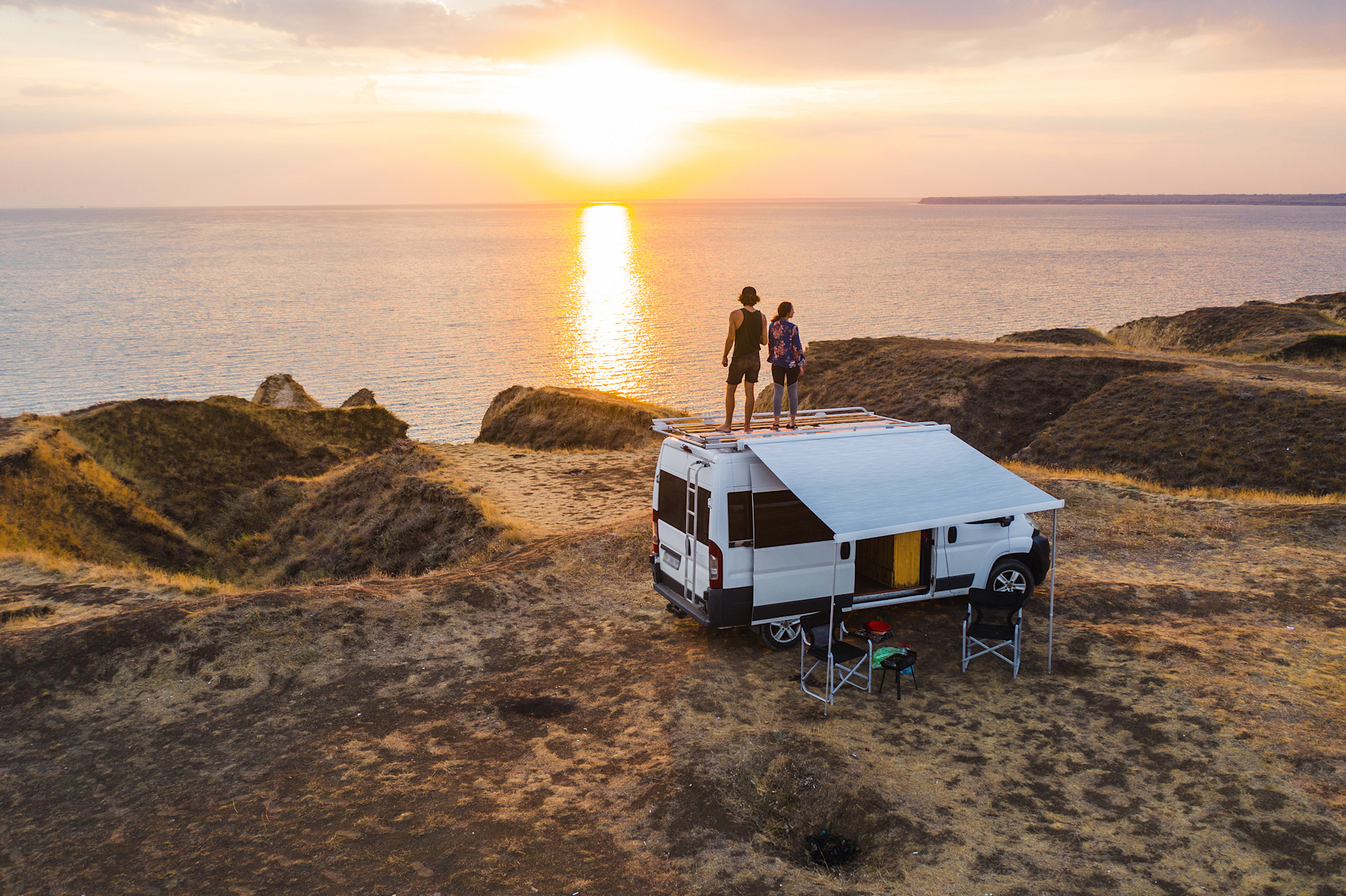 Couple stood on the top of a campervan watching the sunset